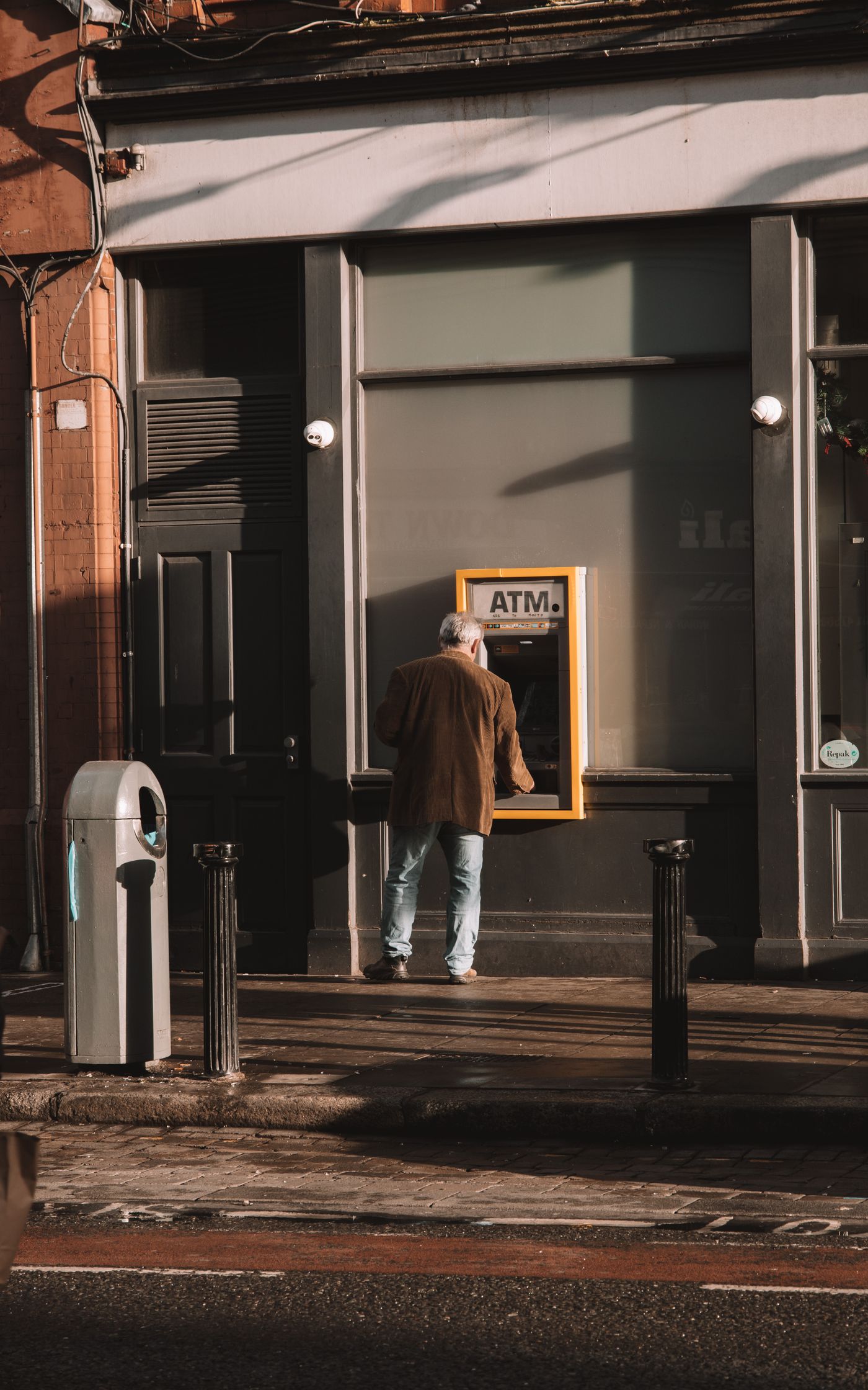 A man using a cash machine set into a wall on a city street in daylight.