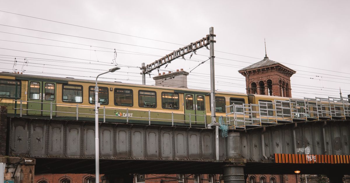 DART train on railway bridge in Dublin with historic tower backdrop.