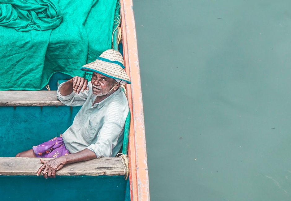 Elderly man in a straw hat relaxing on a colorful wooden boat near blue-green water.
