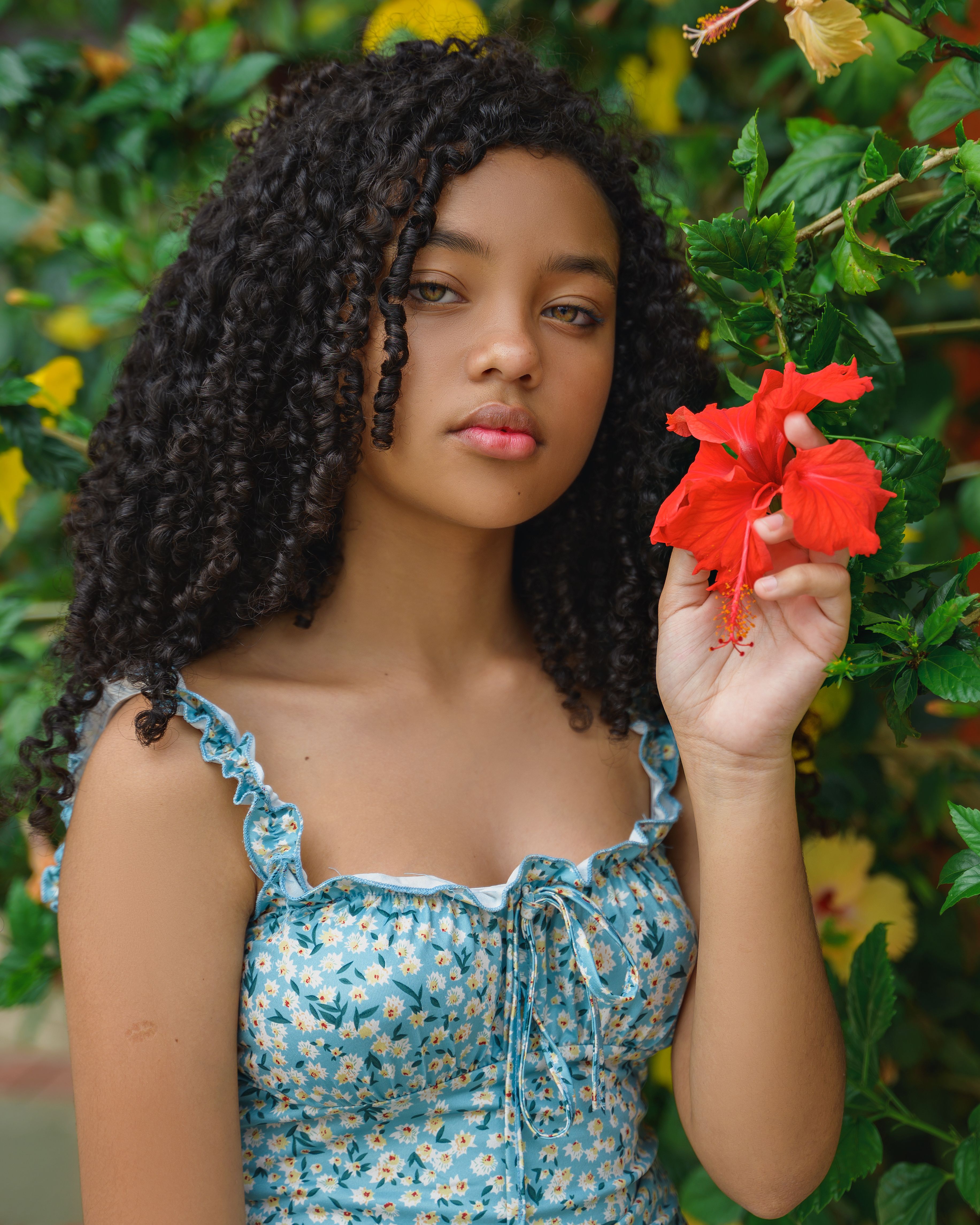 Young woman with curly hair holding a vibrant red flower outdoors.