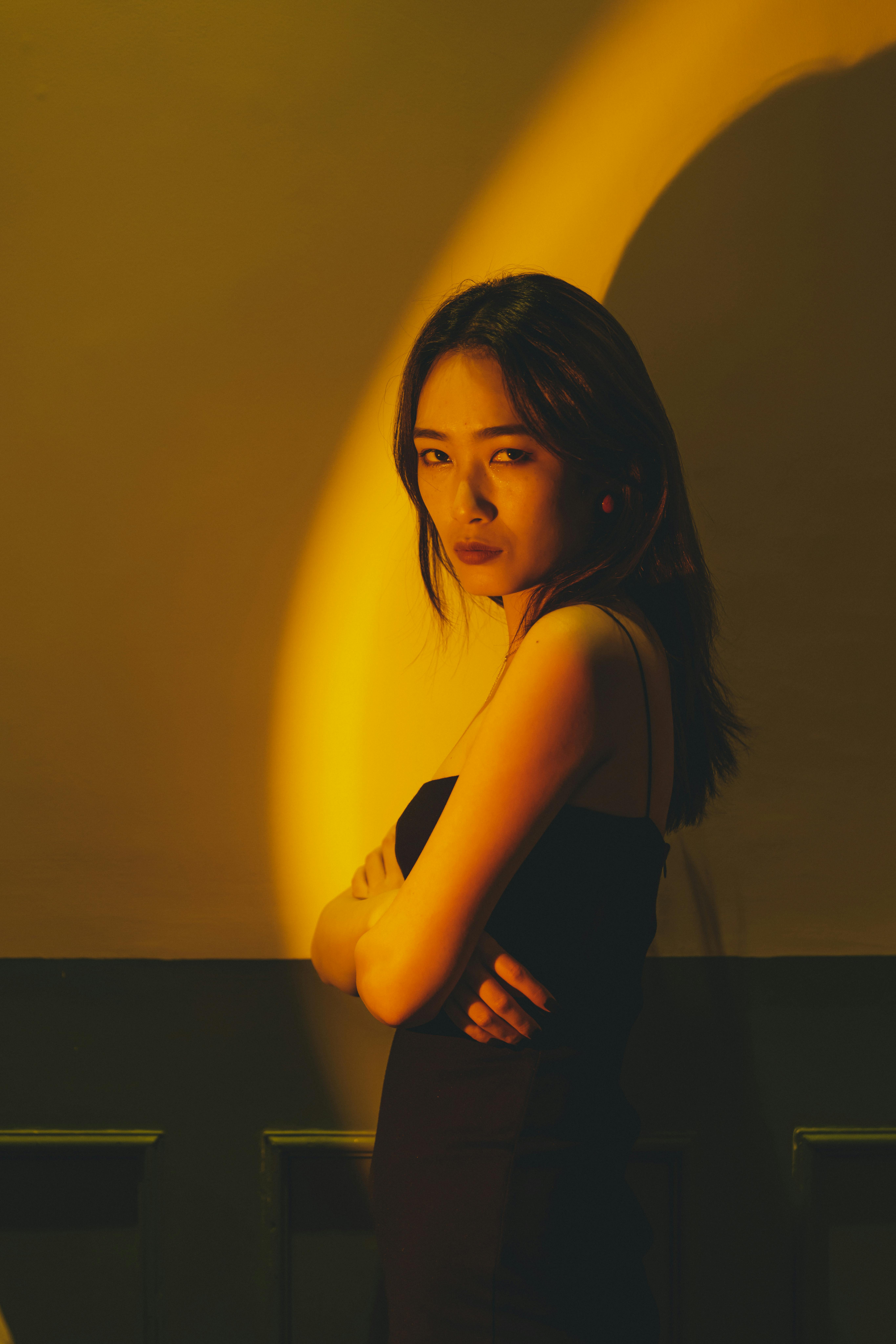A fashionable woman poses with crossed arms under dramatic lighting, showcasing elegance and style.
