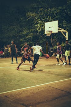 Dynamic scene of men playing basketball on an outdoor court at night.