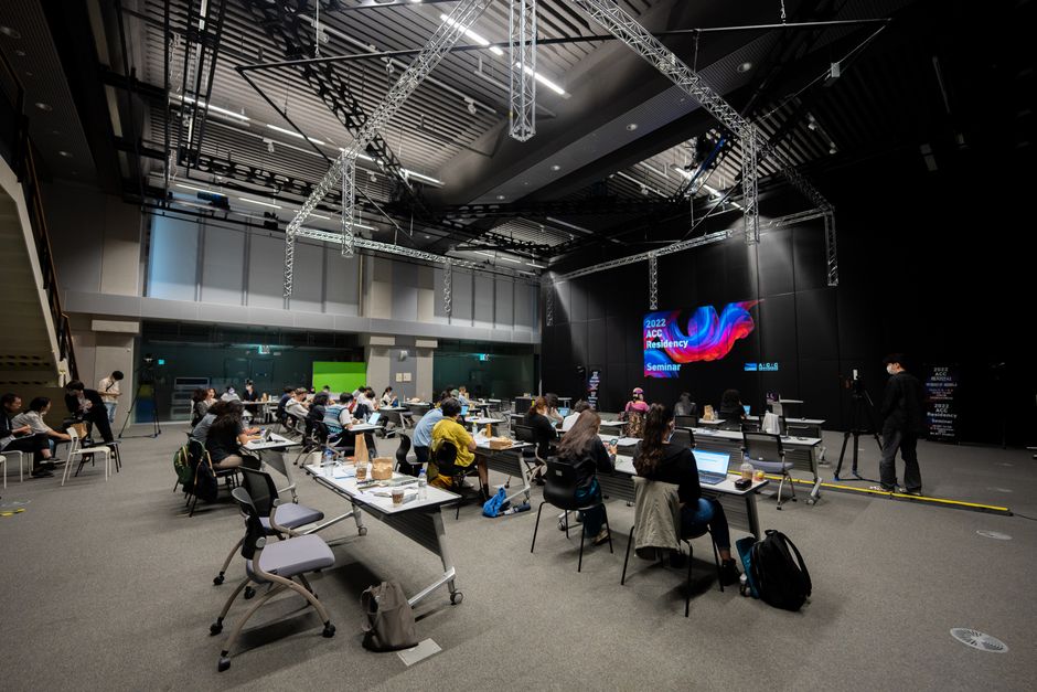 A diverse group attending an educational seminar with screens and seating indoors, highlighting collaboration.