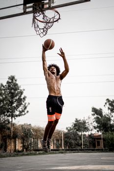 Shirtless man executing a powerful basketball dunk on an outdoor court during the day.