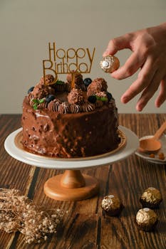 Chocolate birthday cake with decoration and hand placing candy, perfect for celebrations.