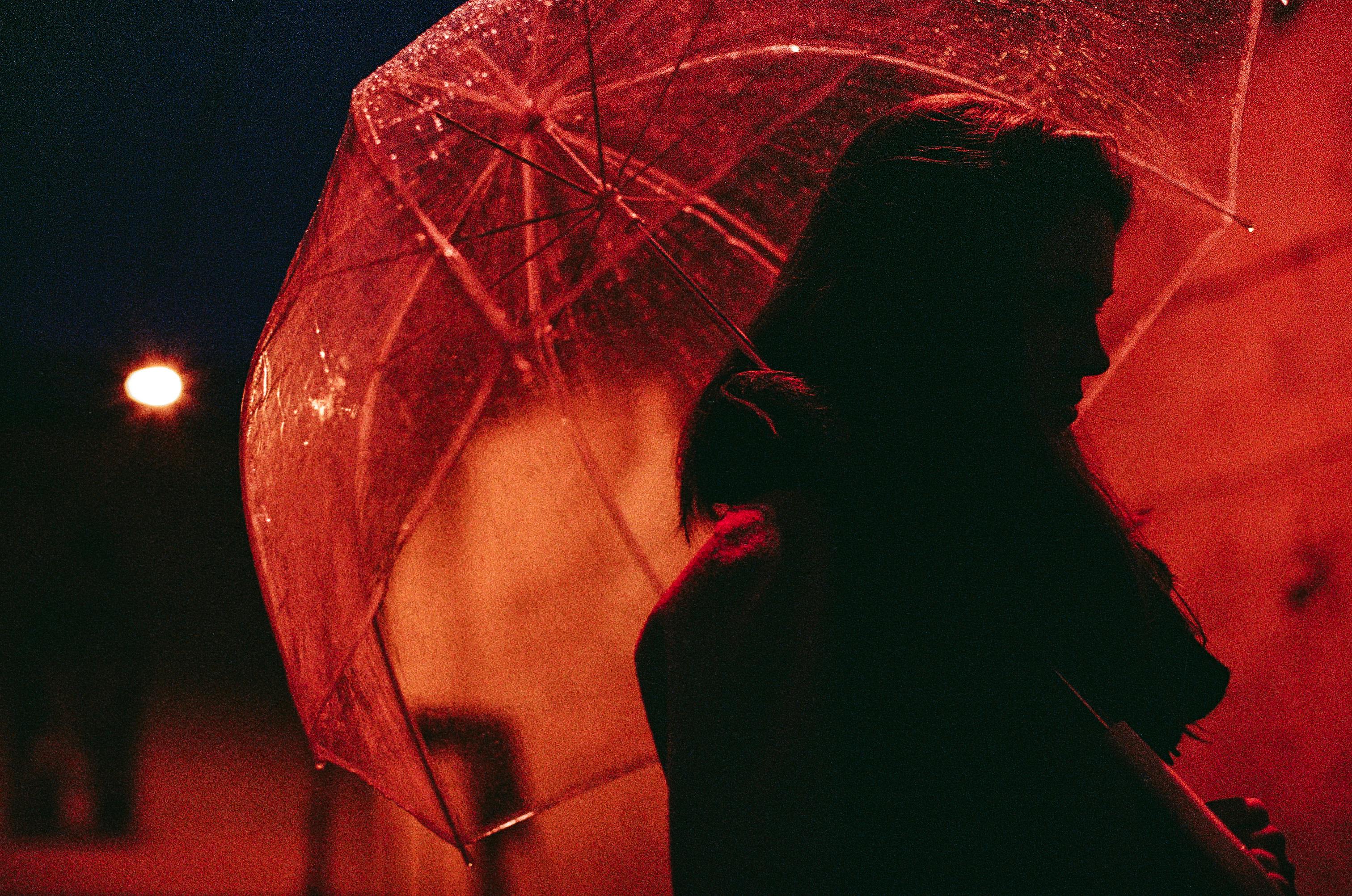Silhouette of a woman with a transparent umbrella under city streetlight at night.