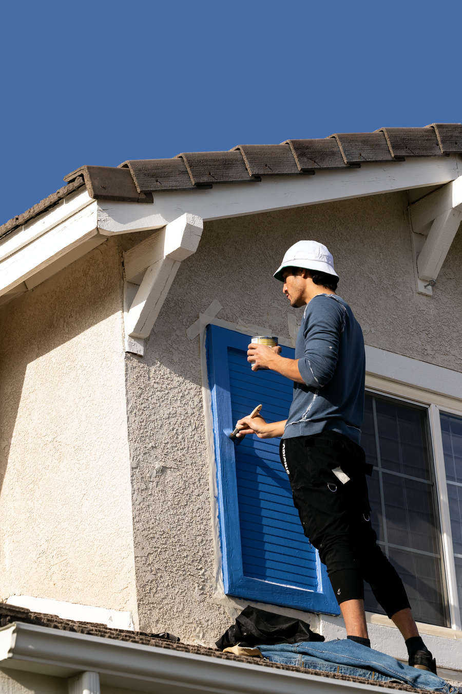 Painter brushing fresh paint onto a house shutter and window trim on a stucco exterior