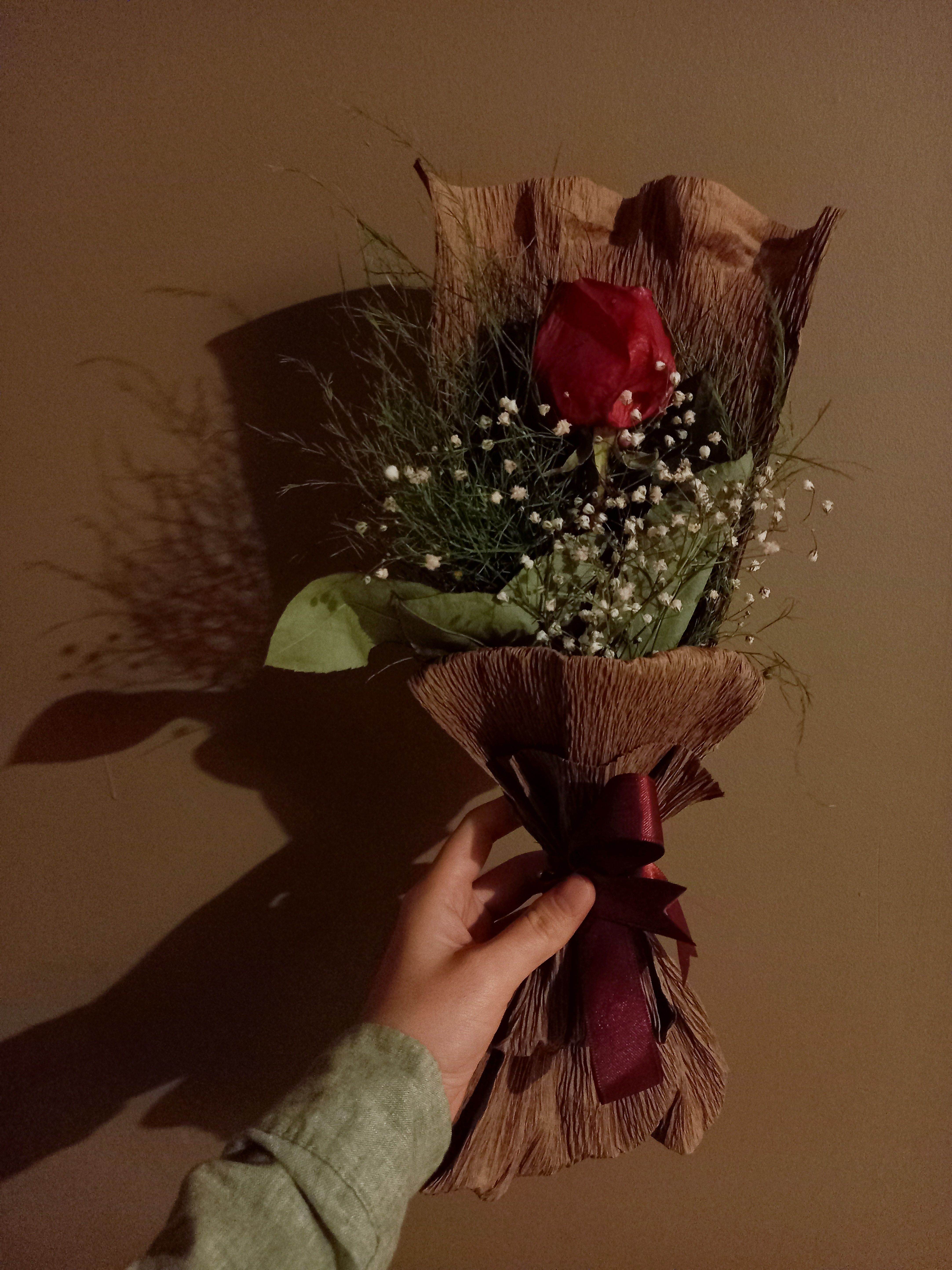 A close-up of a hand holding a red rose bouquet wrapped in a natural brown wrapper on a dark background.