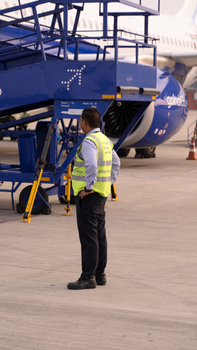 Airport ground staff member in reflective vest standing on tarmac, overseeing aircraft operations.
