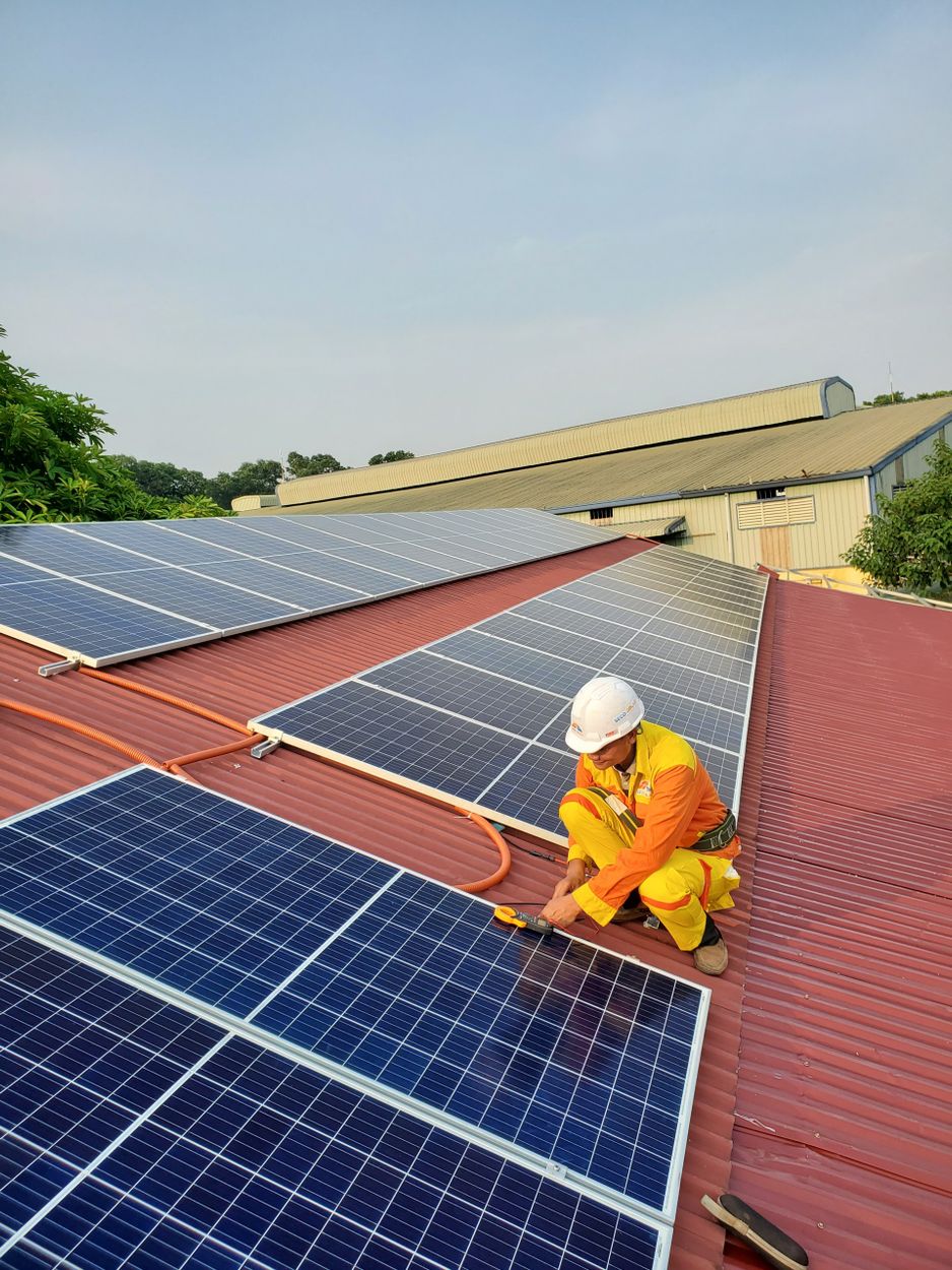 Technician installing rooftop solar panels under a clear sky
