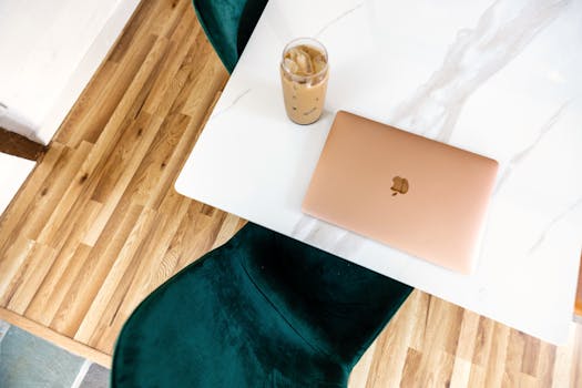 A top view of a contemporary workspace with a laptop, iced coffee, and a velvet chair.