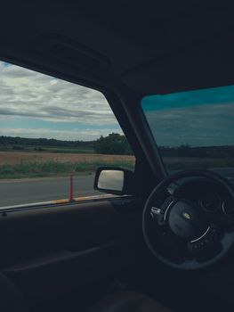 Interior car view with countryside road and field backdrop.