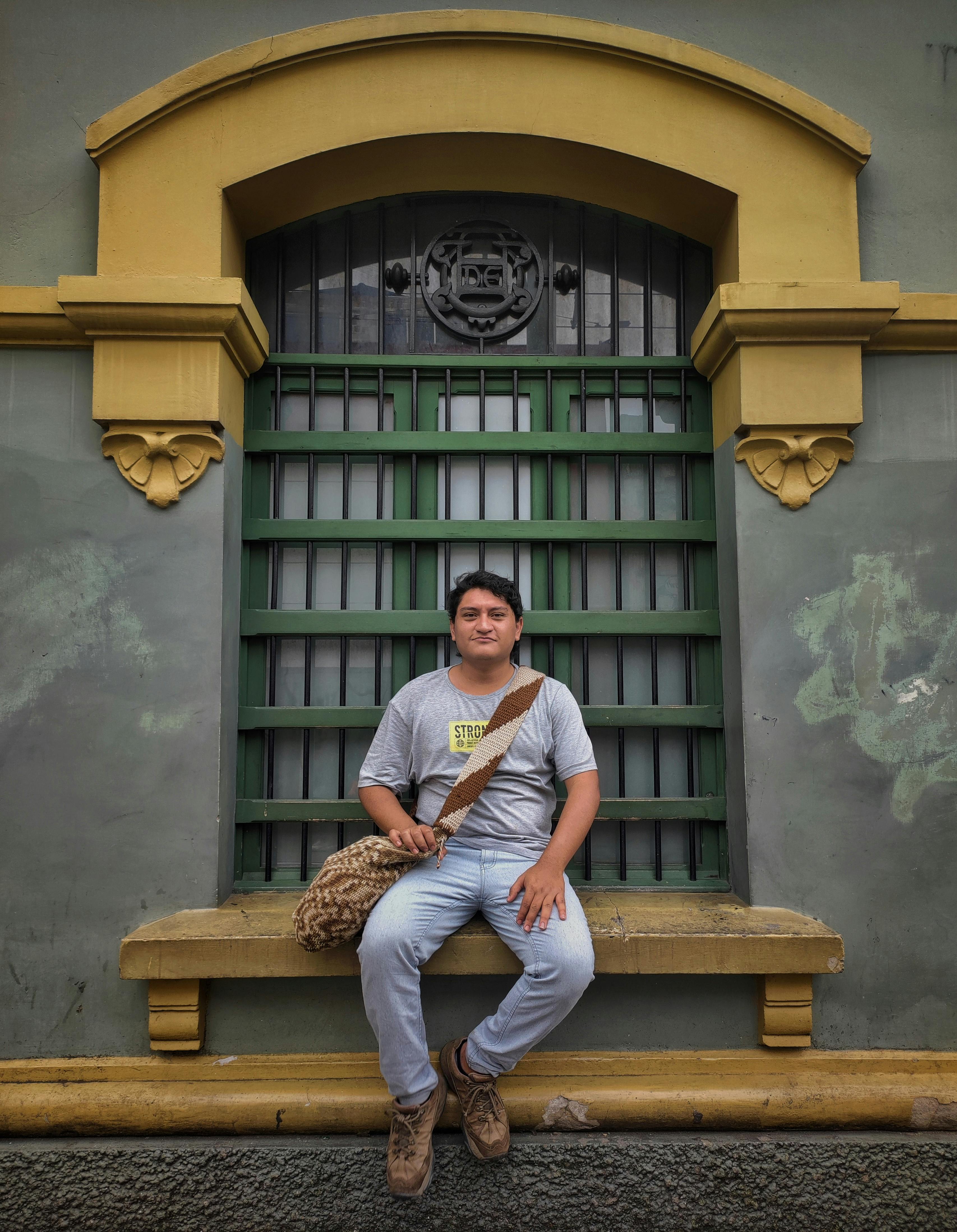 Casual man sitting on an ornate windowsill in Medellín, Colombia, showcasing urban architecture.