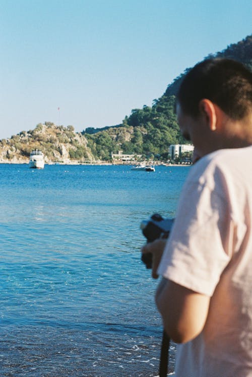 Man Looking at His Camera while Standing Near Body of water