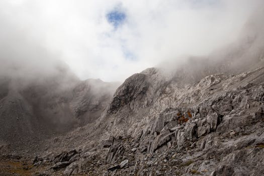 Dramatic view of rocky slopes of Yulong Mountain shrouded in mist, with clouds descending over rugged peaks.