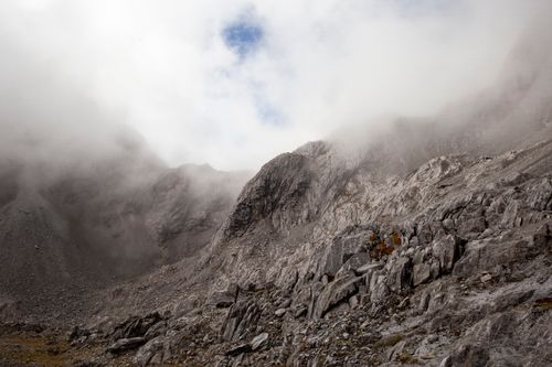 Free Dramatic view of rocky slopes of Yulong Mountain shrouded in mist, with clouds descending over rugged peaks. Stock Photo