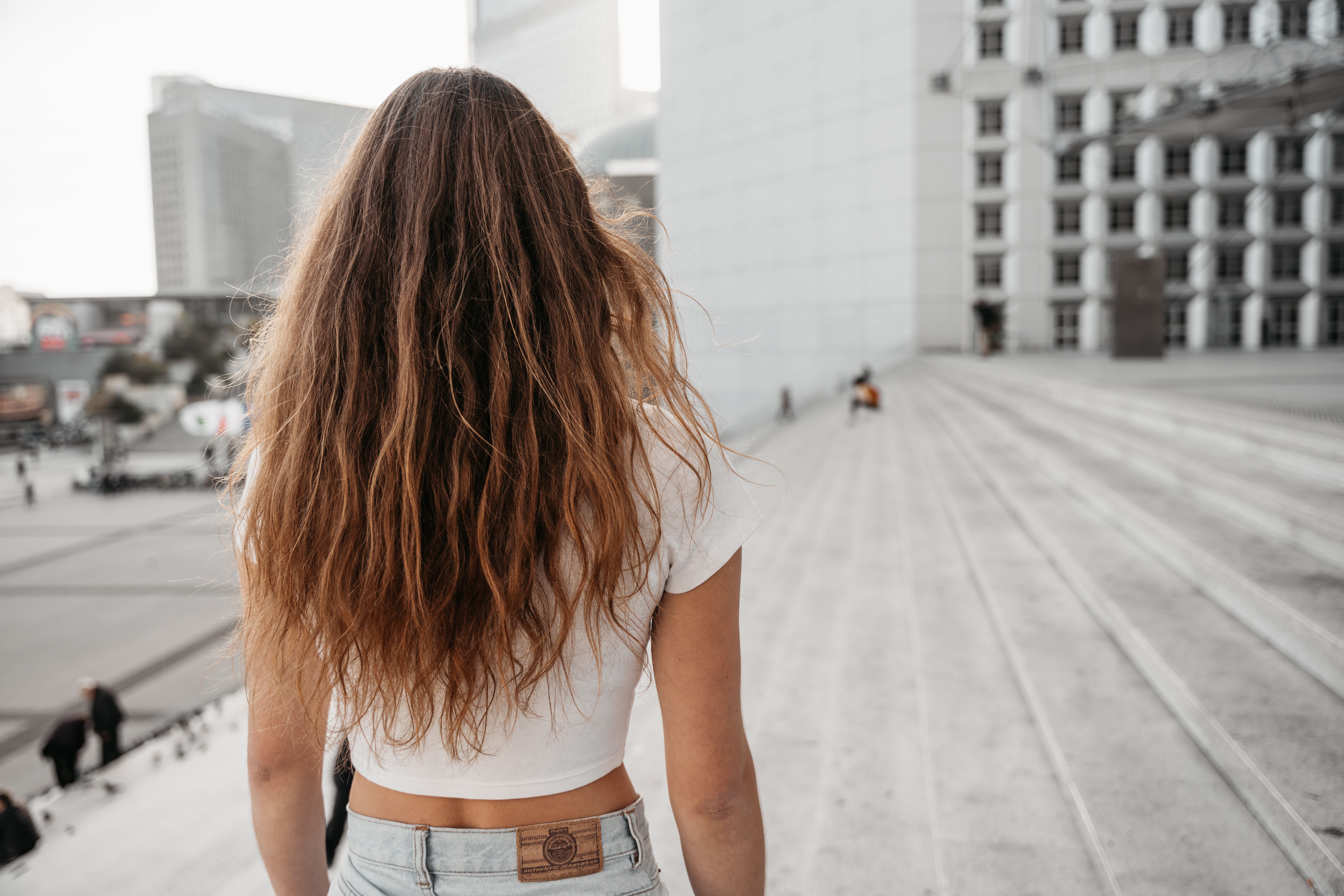Woman with long brown hair walking up concrete steps in an urban setting.