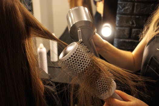 Close-up of a hairstylist drying and styling long hair with a round brush in a salon.