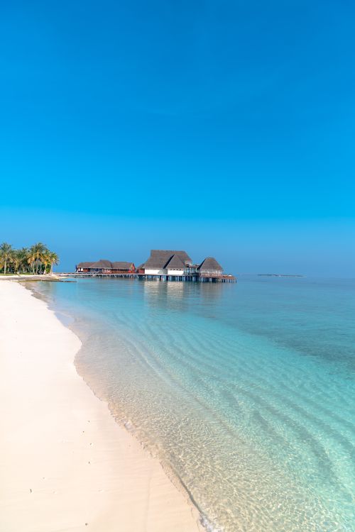 Free Idyllic tropical beach with overwater bungalows and clear blue ocean waters at sunrise. Stock Photo