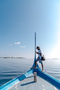 Man standing alone on a blue boat with clear ocean and sky. Perfect for adventure themes.
