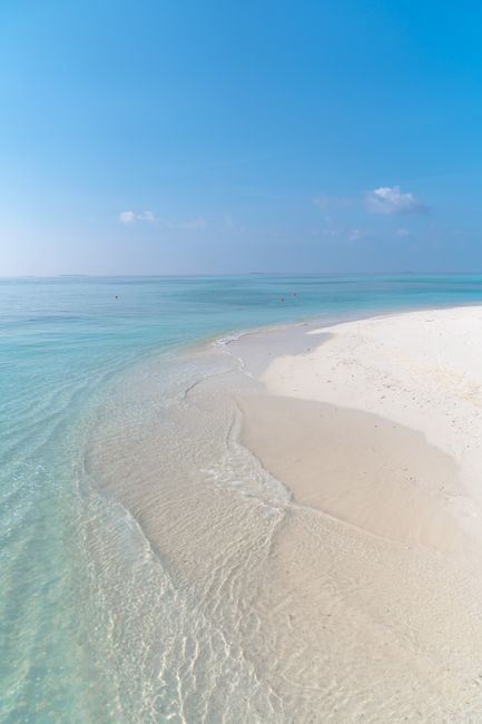 Tranquil beach scene with crystal-clear water, white sand, and bright blue sky, perfect for relaxation and vacation vibes.