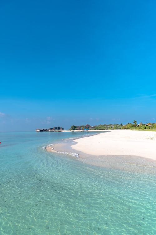 Free Serene white sand beach with turquoise waters under a vibrant blue sky, perfect for relaxing escapes. Stock Photo