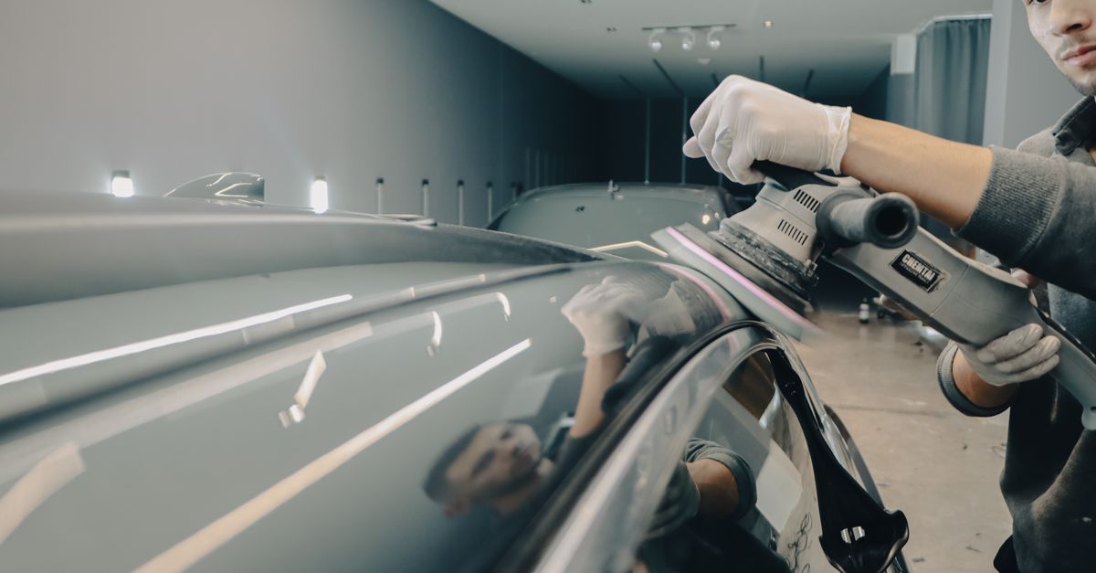 Worker using electric polisher on car roof for a shiny finish in an auto workshop.