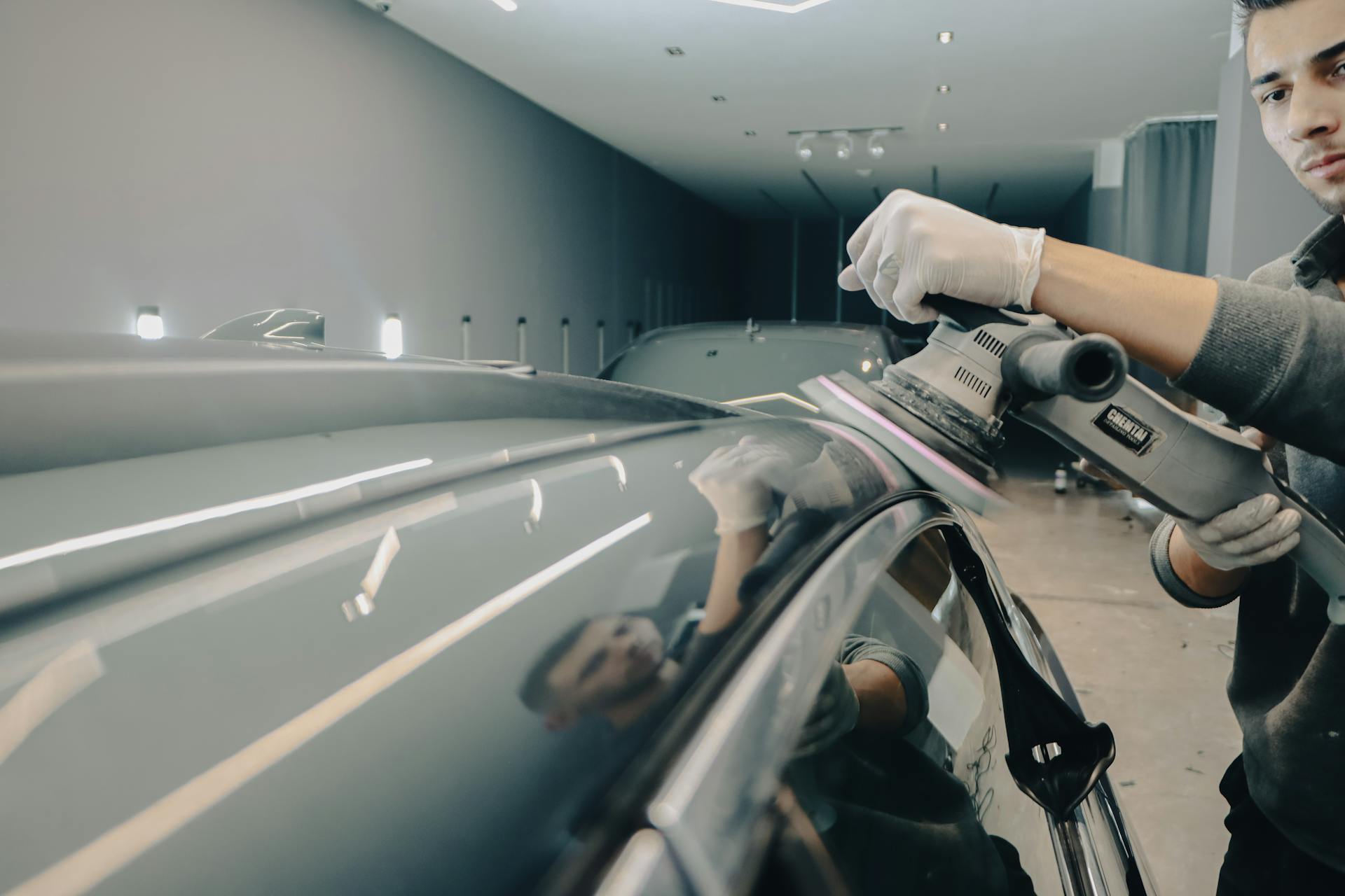 Worker using electric polisher on car roof for a shiny finish in an auto workshop.