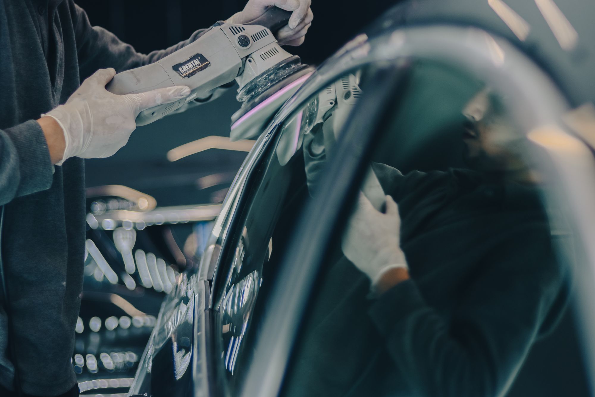 Detailing professional using a dual-action polishing machine on glossy dark automotive paint