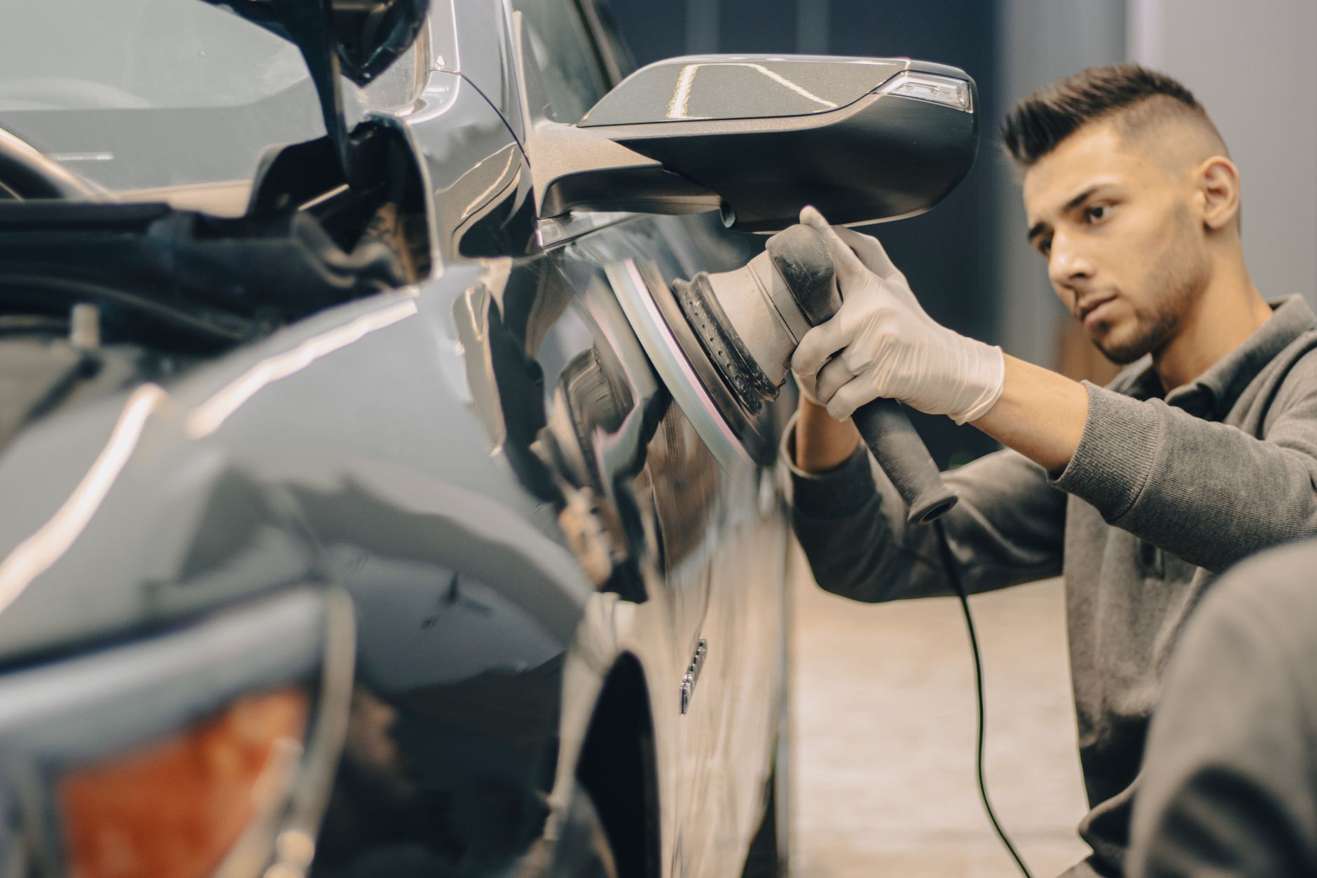 A focused worker polishes a vehicle with precision indoors.