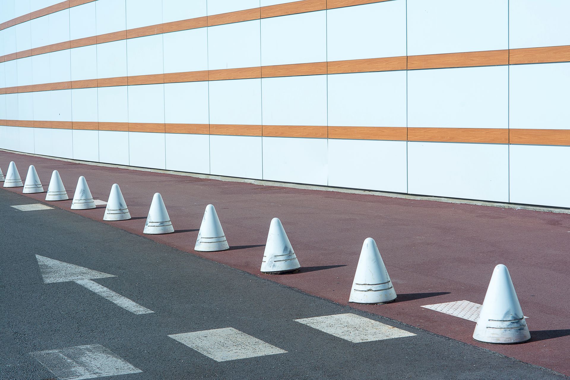 A row of white traffic cones placed on a street near a modern building, highlighting control and safety.