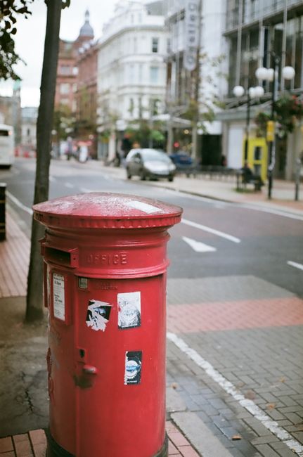 A vibrant red mailbox stands on a city street in Belfast, UK.