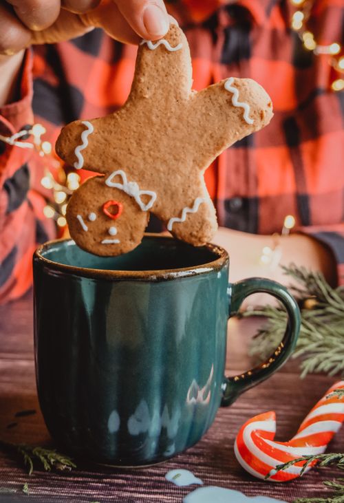 Free A gingerbread man being dipped into a teal mug, evoking holiday cheer with Christmas decor. Stock Photo