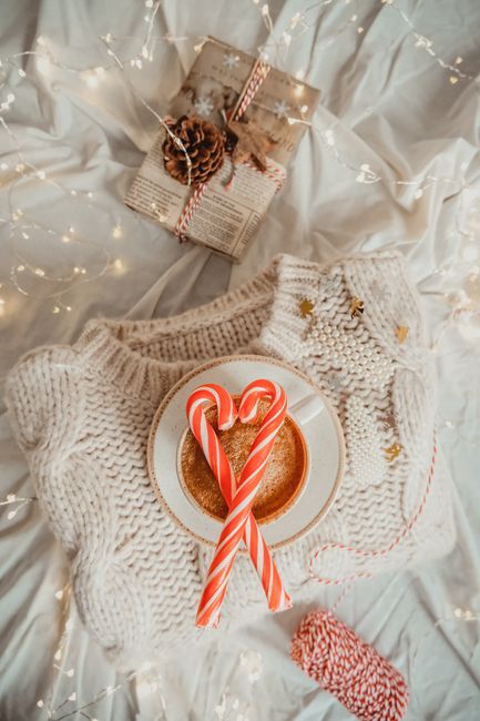Cozy winter coffee setup with candy canes on a sweater, surrounded by festive lights and gift wrap.