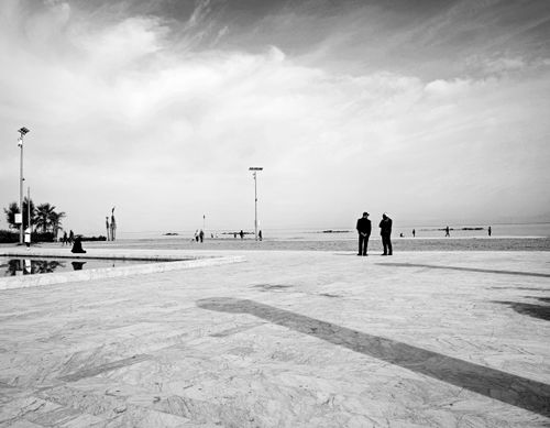 Free Monochrome scene of a beachfront with people walking and talking, set against the sea. Stock Photo