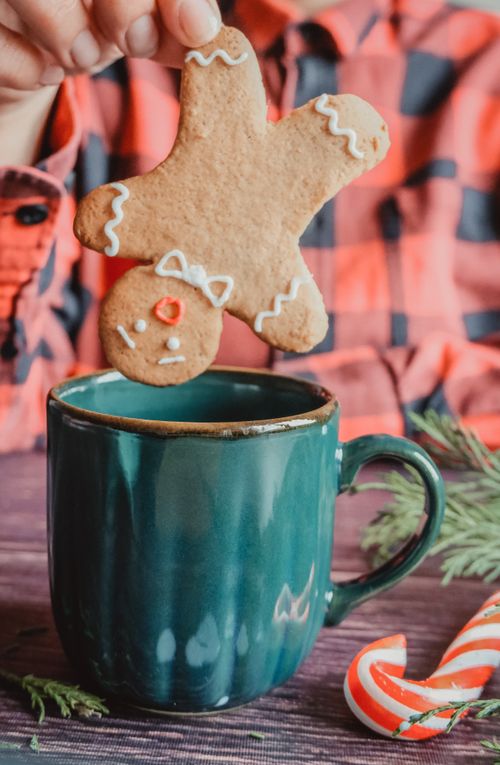 Free Cozy holiday scene with a gingerbread cookie held over a mug, festive decorations add charm. Stock Photo