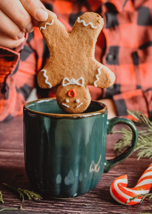 Free Gingerbread cookie dipped in a mug of hot drink, evoking holiday warmth. Stock Photo