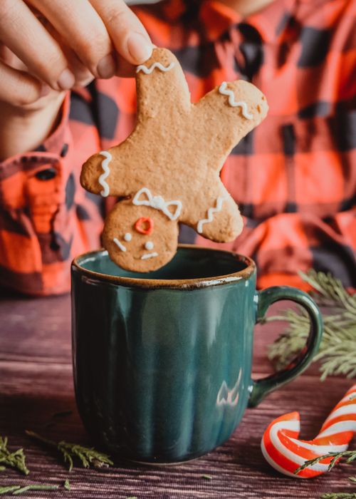 Free Festive gingerbread man cookie being dipped into a green mug, evoking holiday spirit. Stock Photo