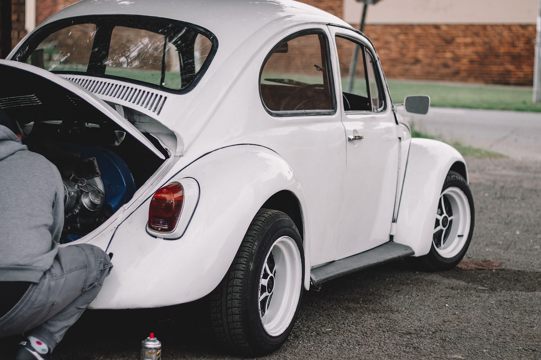 A mechanic working on a classic white Volkswagen Beetle engine outdoors.