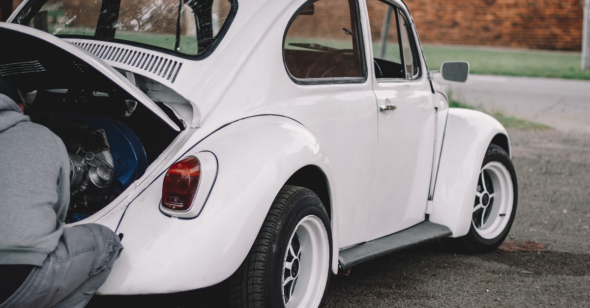 A mechanic working on a classic white Volkswagen Beetle engine outdoors.