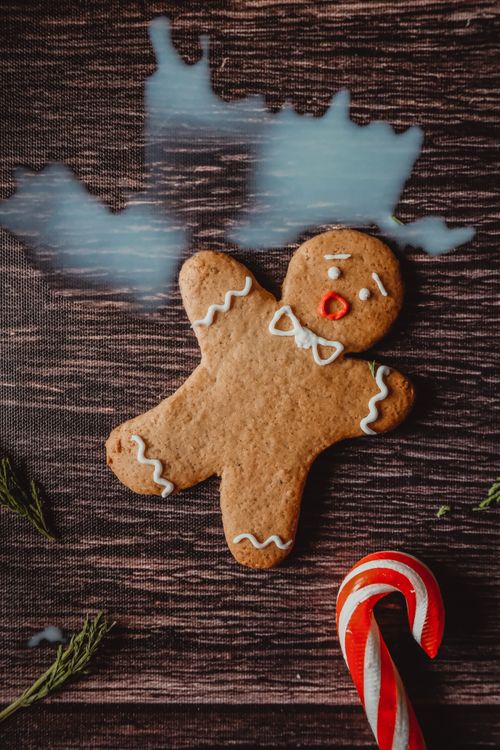 Free Close-up of a gingerbread man cookie beside a candy cane on a wooden table, evoking a Christmas atmosphere. Stock Photo