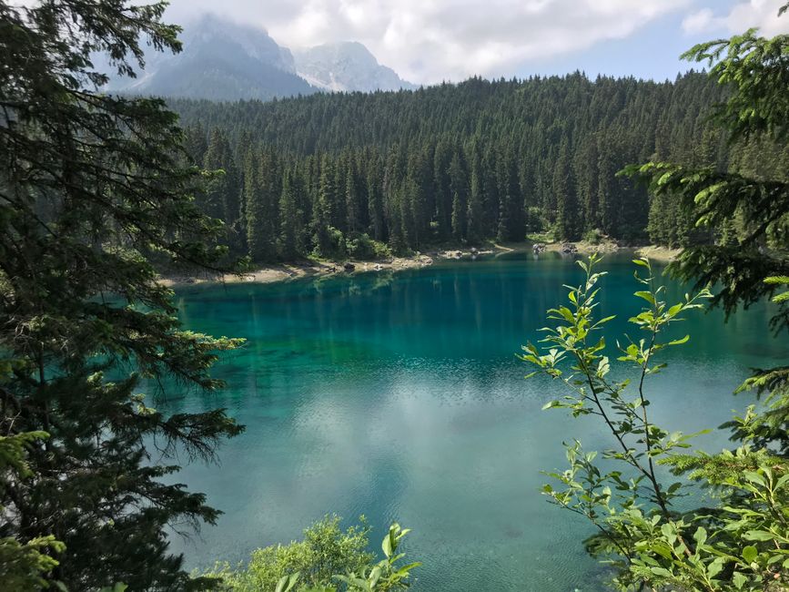 Breathtaking view of a lake surrounded by dense forest in Welschnofen, Italy, under a bright sky.