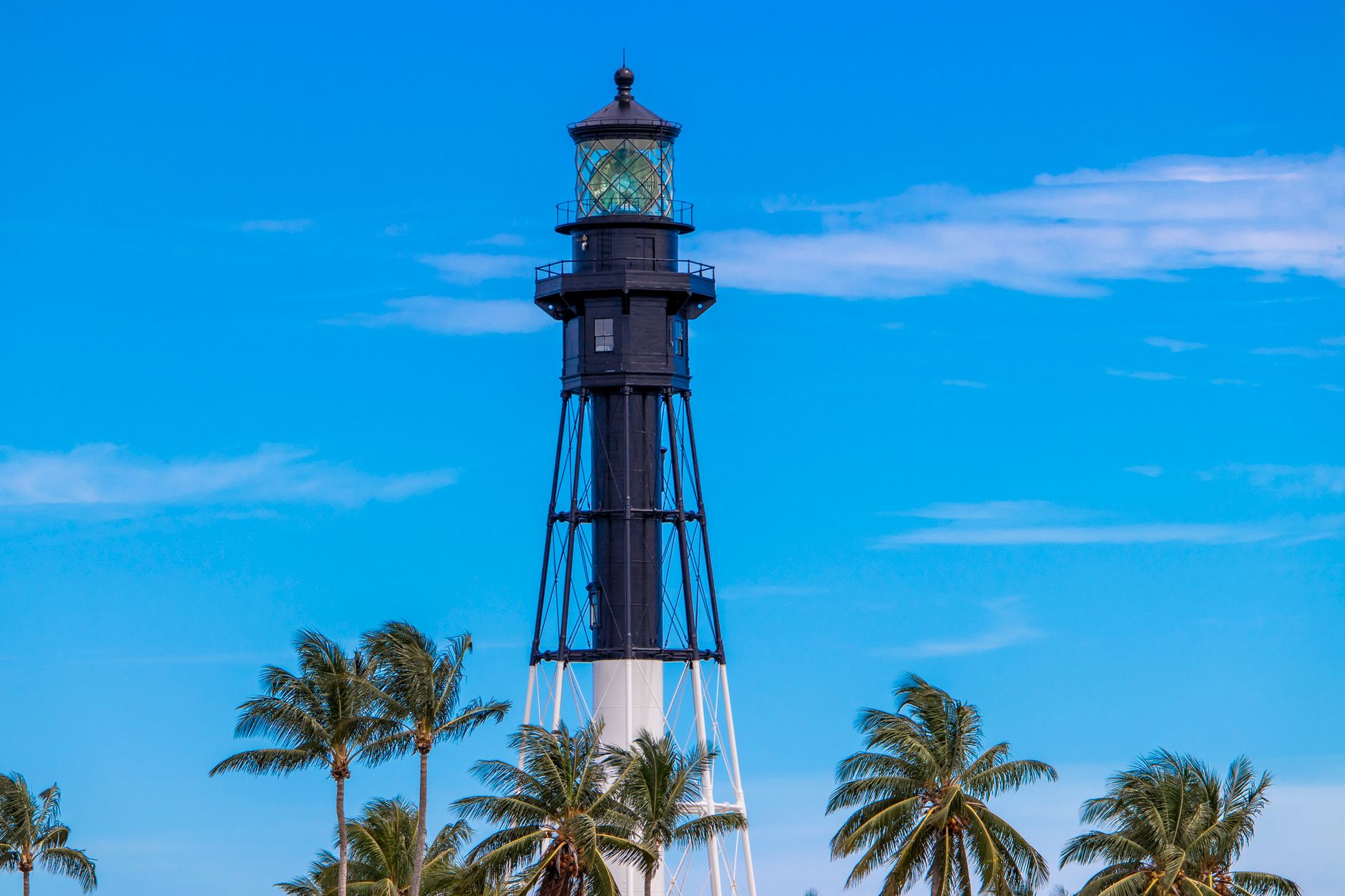 A striking lighthouse surrounded by palm trees under a clear summer sky.