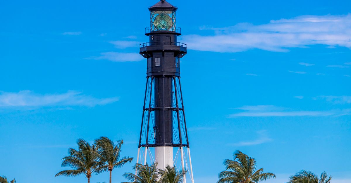 A striking lighthouse surrounded by palm trees under a clear summer sky.
