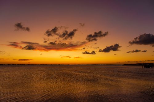 Free A breathtaking view of a serene sunset over the ocean with vibrant orange skies and scattered clouds. Stock Photo