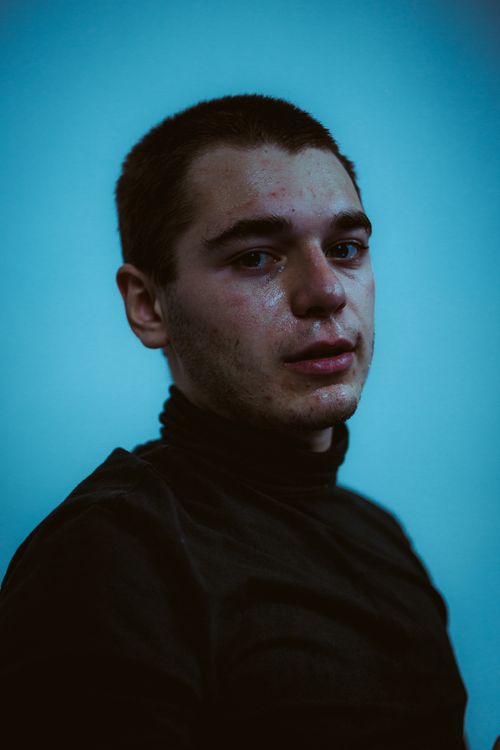 Free A dramatic portrait of a sweaty young man in a black turtleneck against a cool blue background. Stock Photo