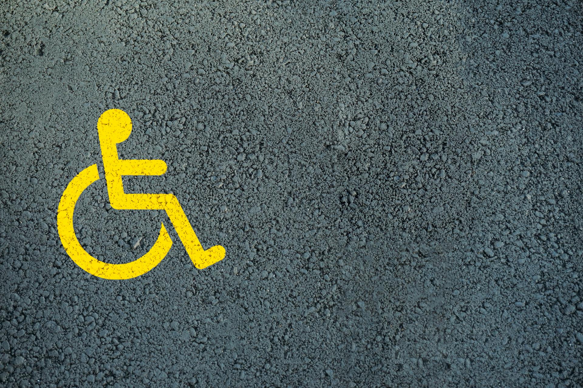 Close-up of a bright yellow disabled symbol on textured asphalt, indicating accessibility.