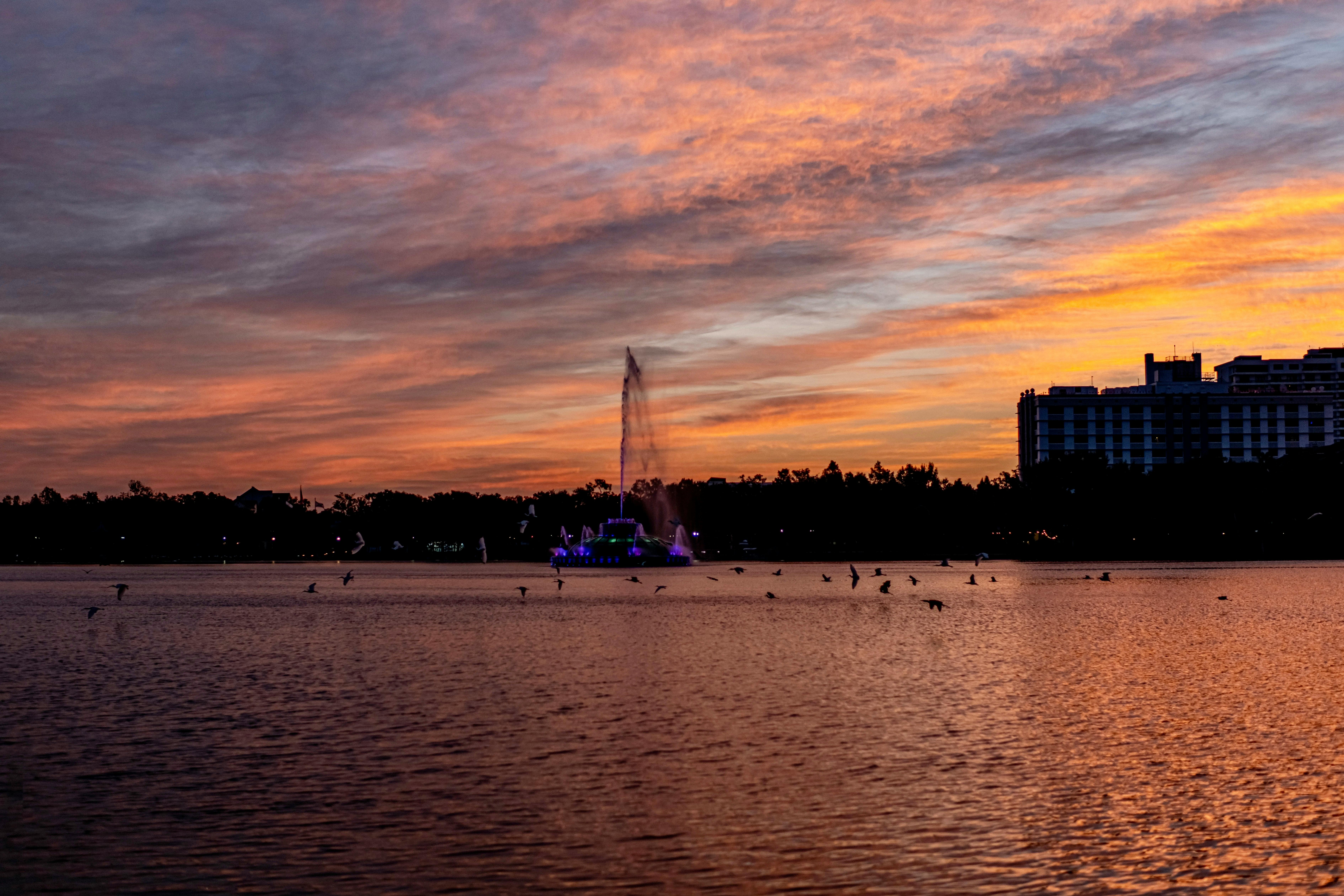 a sunset over a lake with a fountain in the middle