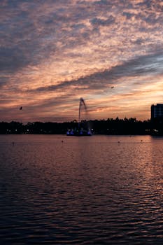 Beautiful sunset over a tranquil lake reflecting the vibrant sky, with a city skyline in the distance.