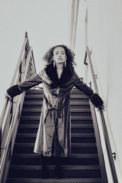 Monochrome Photo of a Woman in a Coat Posing on the Stairs